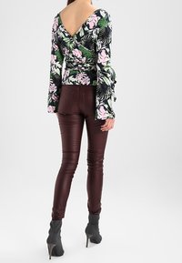 Blouse à manches longues avec imprimé floral et dos en V profond, associée à un pantalon brillant bordeaux ajusté et des bottines noires à talons hauts.
