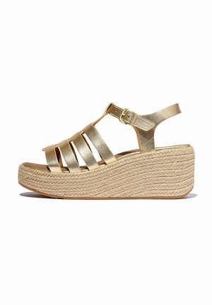 Les sandales à wedge métalliques dorées présentent plusieurs brides, un design à T et une semelle en plate-forme en jute. Boucle ajustable à la cheville.