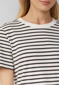 Gestreiftes Kurzarm-T-Shirt in Weiß und Dunkelbraun. Es hat einen runden Halsausschnitt und eine weiche Textur mit abwechselnd dickeren und dünneren Streifen.