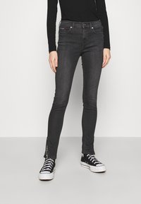 Vaqueros ajustados negros con una textura de denim suave, detalles de cremallera lateral en los tobillos y un diseño ceñido. Combinados con zapatillas negras.