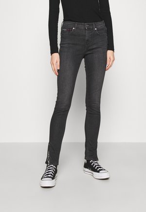 Vaqueros ajustados negros con una textura de denim suave, detalles de cremallera lateral en los tobillos y un diseño ceñido. Combinados con zapatillas negras.
