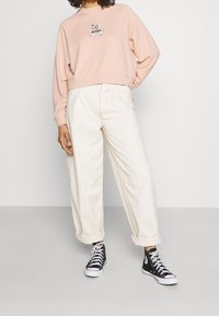 Rosa sweatshirt med ett kaninmotiv, i kombination med off-white vida byxor och svarta högsäkerhetsskor. Mjuk textur, avslappnad passform.