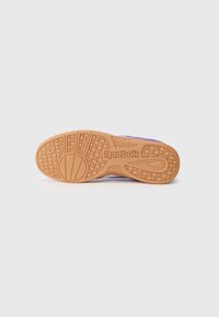 Gumijas zole ar ģeometrisku rakstu, apakšā redzams "Reebok" logo; tekstūrēta brūngana krāsa. Augšējā daļa nav redzama.