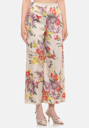 Donna che indossa pantaloni crema a gamba larga e vita alta con motivo floreale rosso, viola, giallo e scarpe slingback beige con tacco.