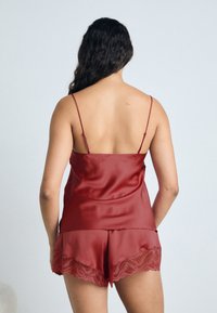 Camisole en satin rouge avec fines bretelles, associé à un short assorti avec un ourlet en dentelle à volants. Texture lisse, design ajusté.