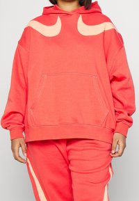 Korallröd hoodie med en stor framficka, med ljus persikofärgade hornformade detaljer på axlarna och ribbade mudd på ärmsluten.