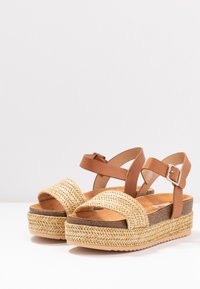 Bruna plattformssandaler i konstläder med vävda strådetaljer; justerbar ankelrem; texturerad yttersula; vadderad innersula.