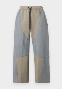 Laza szabású nadrág szürke és bézs színkombinációban, texturált anyagpanelek és zsinórral állítható derékkal. Nike logó az egyik oldalon.