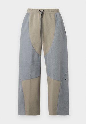 Pantalones de corte relajado con una combinación de colores gris y beige, que presentan paneles de tela texturizada y una cintura con cordón. Logo de Nike en un lado.