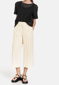 Haut noir en tricot à manches courtes avec une coupe ample, associé à un pantalon large beige clair avec une taille élastique, et des sandales à plateforme noires.