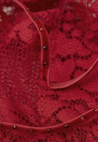 Rød blonde stof med indviklede mønstre, der har en struktureret overflade og en satinbånd prydet med små røde rhinsten.