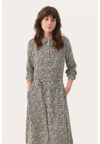 �Čierno-biel dress s kvetinovým vzorom, s golierom, dlhými rukávmi a prednými vreckami. Obsahuje zúžený pás a splývavú sukňu.