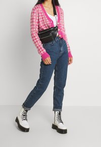 Vaaleanpunainen ja valkoinen ruutukuvioinen neuleeseen V-pääntiellä, musta olkalaukku, siniset korkeavyötäröiset farkut ja valkoiset nauhalliset nilkkurit.