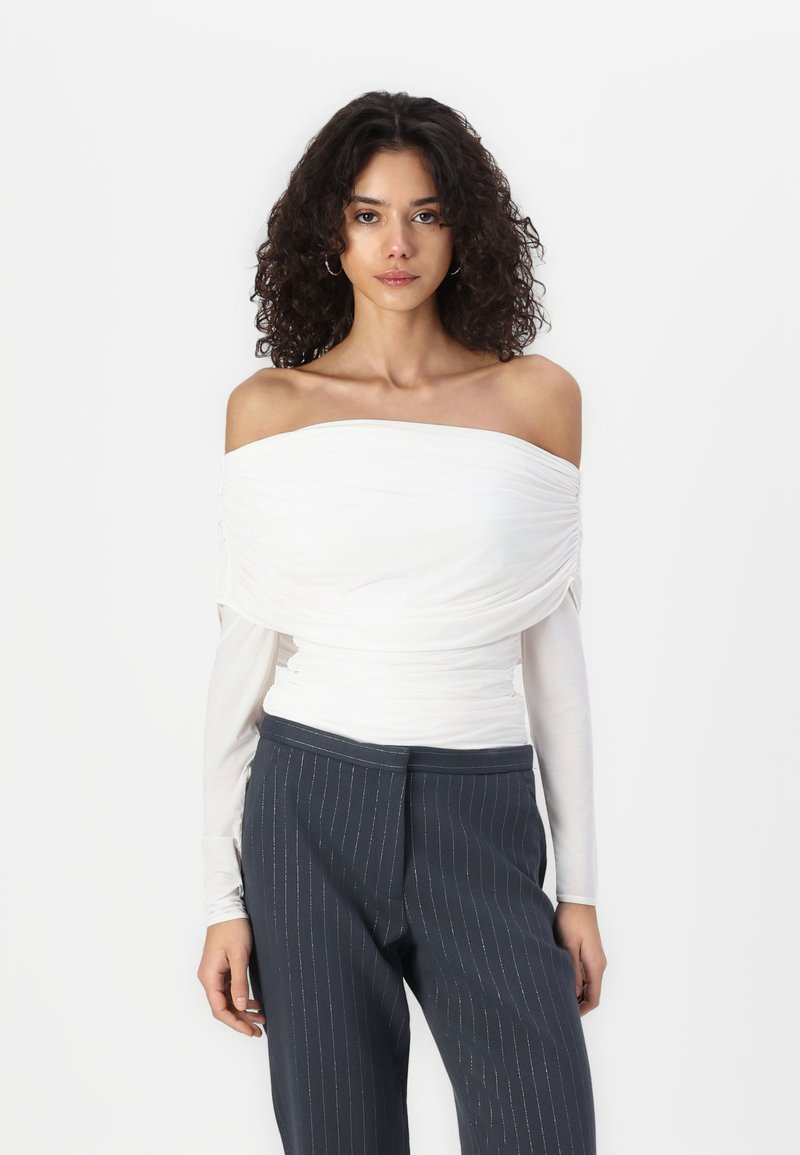 Top blanco sin mangas con drapeado texturizado, superpuesto sobre mangas largas. Combinado con pantalones de rayas finas en azul marino oscuro.