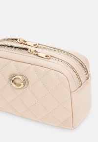Pochette cosmetica in pelle beige trapuntata con doppia chiusura a zip dorata e una decorazione con emblema dorato sulla parte frontale. Finitura testurizzata con motivo a diamante.