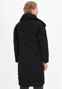 Căciulă neagră căptușită, cu un model în valuri, guler înalt și mâneci lungi. Materialele par moi, cu o textură netedă, oferind căldură.