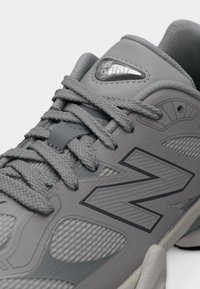 Γκρι αθλητικό παπούτσι New Balance με υφασμάτινο συνθετικό επάνω μέρος με υφή, έντονο λογότυπο, στρογγυλεμένη μύτη και κορδόνια στο ίδιο χρώμα. Ελαφρύ σχέδιο.