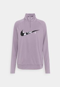 Vaaleanliila, pitkähihainen Nike-pulloveri, jossa on korkea kaulus, puolipitkä vetoketju ja musta logo sekä teksti rinnassa. Pehmeä kangaspinta.