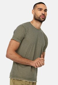 Kortærmet t-shirt i et grønt og sort geometrisk mønster, med rund hals og en blød, struktureret stof.