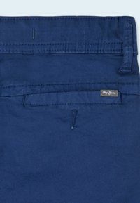 Pantalones azul marino con una textura suave, que cuentan con un bolsillo trasero y una pequeña etiqueta de logo. La cinturilla presenta un detalle de costura.