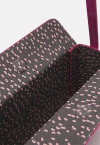 Czarny materiał wykończeniowy z różowym wzorem w kropki, charakteryzujący się gładką teksturą i różowymi brzegami. Na powierzchni widoczne są dwa okrągłe akcenty.