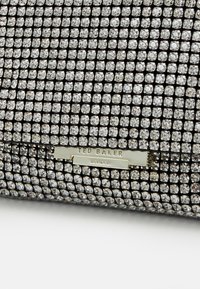 Sort clutch-taske dækket med små, klare rhinsten. Har en guld "Ted Baker London" logo-plade. Glat tekstur med rektangulær form.