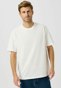 Hvid bomulds t-shirt med korte ærmer, rund hals og løs pasform. Kombineret med blå denimshorts. Ensfarvet design uden synlige mønstre eller detaljer.