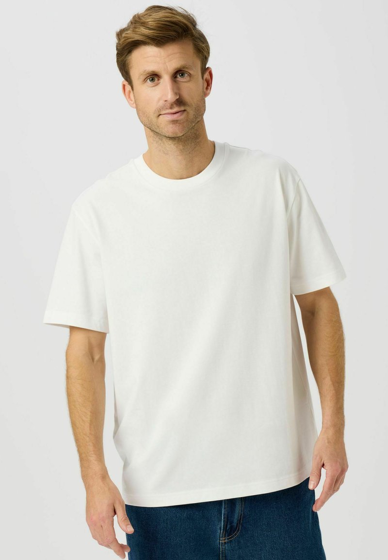 Hvid bomulds t-shirt med korte ærmer, rund hals og løs pasform. Kombineret med blå denimshorts. Ensfarvet design uden synlige mønstre eller detaljer.