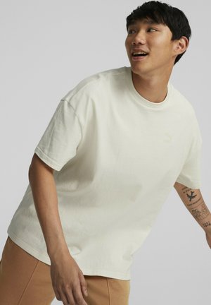 Cremefarvet bomulds-t-shirt med korte ærmer, rund halsudskæring og et lille logo tæt på brystet. Glat tekstur og afslappet pasform.