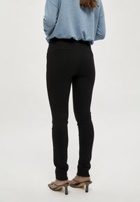 Svarta tights i elastiskt material med hög midja och minimalistisk design, kombinerade med öppna klackar.