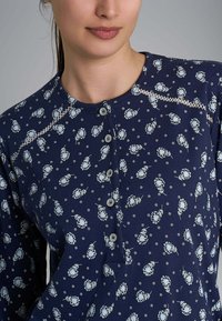 Top in cotone blu navy con motivi floreali e circolari, caratterizzato da un collo con bottone e cuciture decorative lungo le spalle.