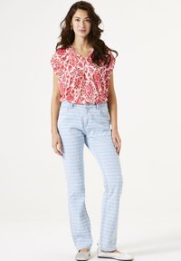 Blusa de rayas rojas y blancas con mangas cortas, combinada con jeans azul claro que presentan un diseño texturizado. La modelo lleva zapatos planos plateados.