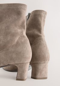 Brown suede ankle boots with a round toe, mid-height block heels, and side zipper. Features reinforced stitching and smooth texture.