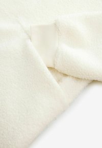 Biała tkanina polarowa z miękką fakturą, z elastycznymi akcentami. Projekt zawiera szew w pobliżu mankietu.