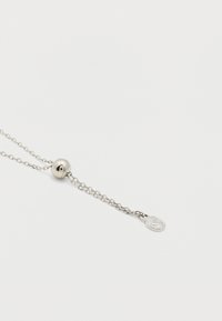 Ασημένιο ρυθμιζόμενο κολιέ με στρογγυλό μετακινούμενο χάντρα και μικρό οβάλ μενταγιόν χαραγμένο με στυλιζαρισμένο γράμμα «S» σε λευκό φόντο.