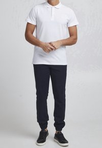 Witte polo shirt met korte mouwen en drie knopen, gecombineerd met marineblauwe joggerbroeken en zwarte sneakers met een witte zool.