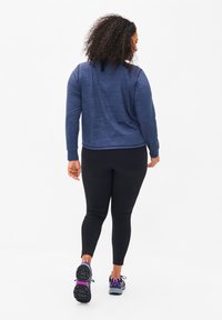 Marineblaues Langarmoberteil mit texturiertem Muster, kombiniert mit schwarzen Leggings und grau-lila Sportschuhen, von hinten betrachtet.