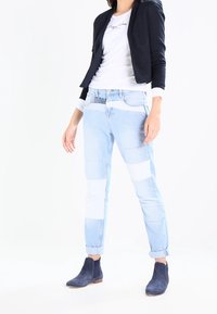 Hellblau Jeans mit einem Patchwork-Design in weißen Abschnitten, kombiniert mit einem marineblauen Blazer und marineblauen Wildleder-Stiefeletten.