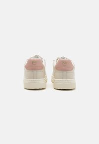 Une paire de baskets blanches montantes avec des languettes de talon roses et un logo doré, vues de l'arrière sur un fond blanc.