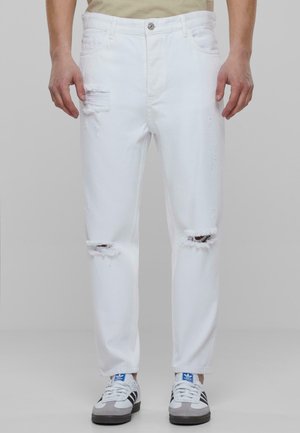 Jean en denim blanc avec déchirures aux genoux, cinq poches et fermeture à bouton. Il présente une coupe droite et des coutures visibles.