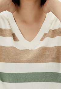 Pull en tricot à col en V et à manches courtes en crème, avec des rayures horizontales beiges et vertes, doté d'une texture douce et d'une coupe décontractée.