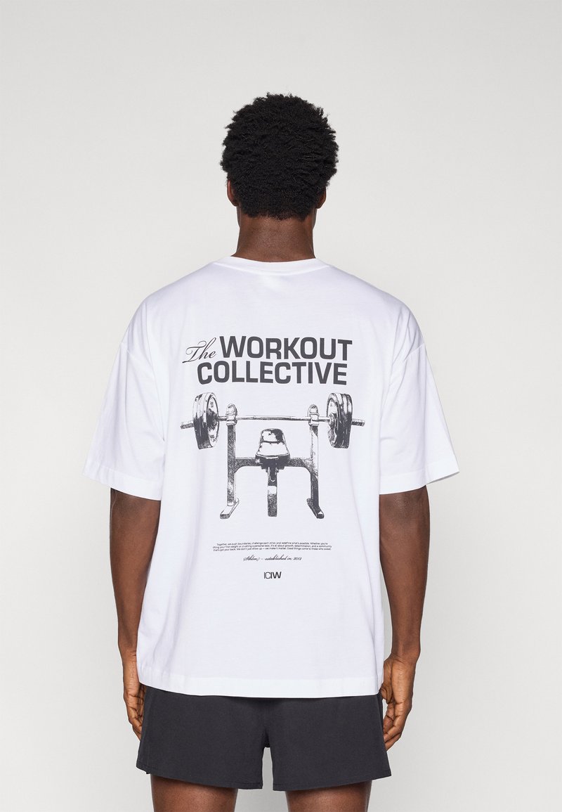 Άσπρο βαμβακερό μπλουζάκι με μεγάλο γραφικό τύπωμα πάγκου άρσης βαρών και μπάρας στη ράχη. Το κείμενο αναγράφει «The WORKOUT COLLECTIVE.»