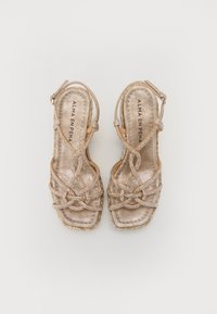 Sandales à lanières en bronze métallique avec un design tissé complexe et une semelle intérieure rembourrée. Présente une sangle à boucle et une semelle plate de style espadrille.