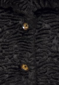 Tissu noir texturé avec un motif ondulé et deux boutons : l'un sombre et brillant, l'autre clair avec une finition naturelle.