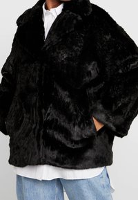 Abrigo de pelo sintético negro con un cuello ancho, corte oversize y superficie texturizada. Cuenta con bolsillos laterales y una silueta relajada.