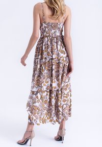 Robe longue à imprimé cachemire dans des tons chauds, avec un corsage froncé, des bretelles fines et un ourlet volanté à volants superposés. Portée avec des talons beiges.