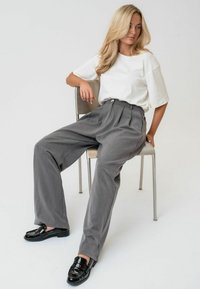 Sive srajčne hlače, bela majica in črne patentne loafers. Obleka ima sproščen kroj in gladke teksture. Minimalističen stil.