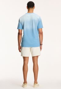 Tricou de culoare albastră deschisă cu efect gradient, mâneci scurte și decolteu rotund, asociat cu pantaloni scurți albi și încălțăminte de culoare deschisă.