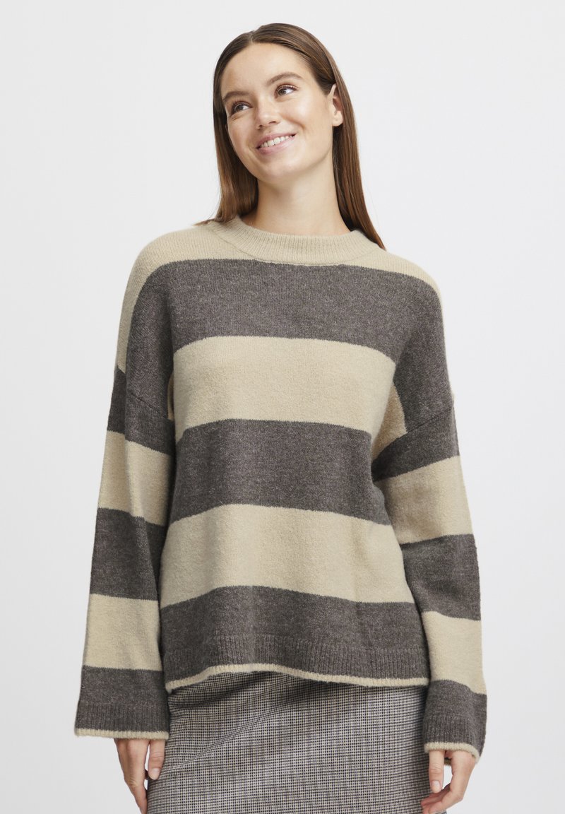Pull rayé en beige et gris foncé, fabriqué à partir d'un matériau tricoté doux. Il présente un col rond et des manches larges et amples. Fini texturé.