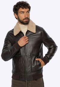 Bruine leren bomberjack met een beige bontkraag, geribde manchetten en tailleband, ritssluiting en twee voorzakken. Soepele textuur.